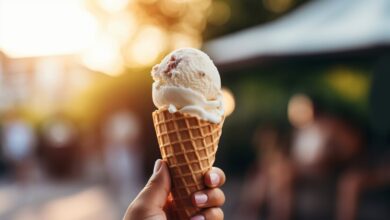 A person holding a cone ice cream outside an ice cream shop